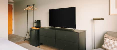 A modern bedroom with a bed, a dresser, a flat-screen TV, a floor lamp, and a framed picture on the wall.