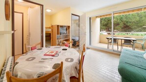 A dining area with a table set for four, a green sofa, and a balcony with outdoor seating. - AS21600-P2Cabin 200m from the beach and parking (LE GRAU DU ROI)