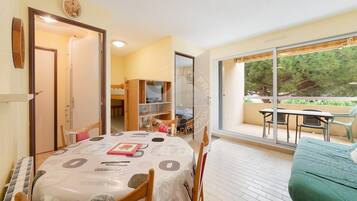 A dining area with a table set for four, a green sofa, and a balcony with outdoor seating.