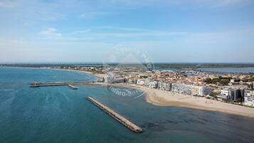 An aerial view of a coastal town with a beach, buildings, and a pier extending into the water.