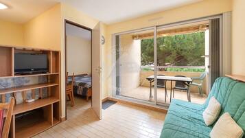 Ein Zimmer mit einem Bett, einem Fernseher auf einem Regal, einem Balkon mit Tisch und Stühlen sowie einem grünen Sofa.