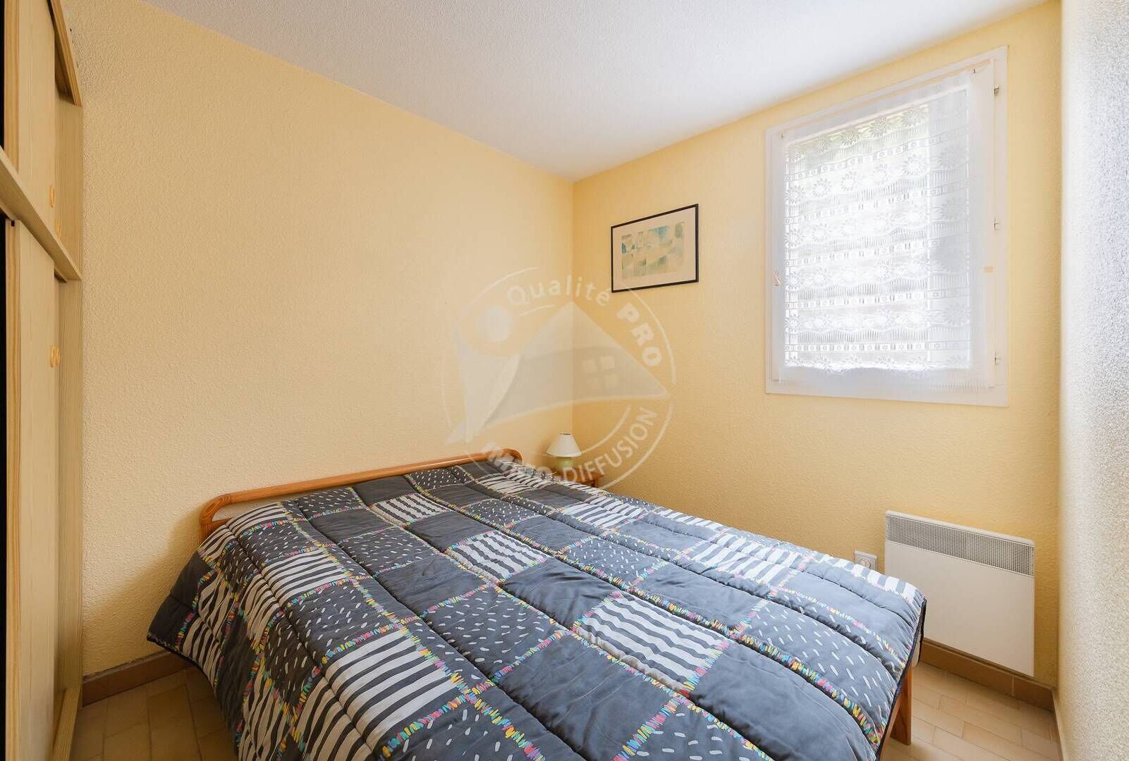 A bedroom with a bed, a radiator, a window with blinds, and a framed picture on the wall.