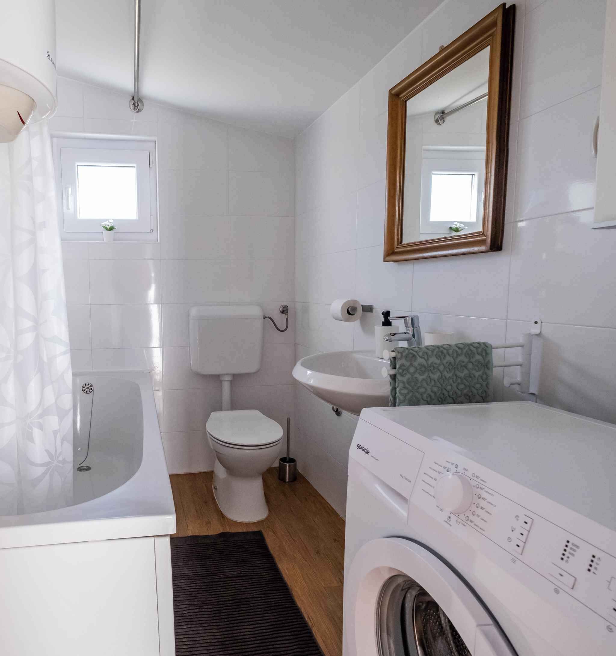 Une salle de bain compacte comprenant une baignoire, des toilettes, un lavabo et un lave-linge.