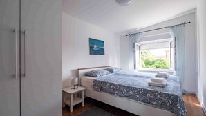 A bedroom with a bed, a nightstand, a window with curtains, and a painting on the wall. - Holiday apartment with air conditioning and barbecue (Peroj)