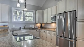 Una cocina moderna con encimeras de granito, electrodomésticos de acero inoxidable, armarios blancos y un ventanal que proporciona luz natural.