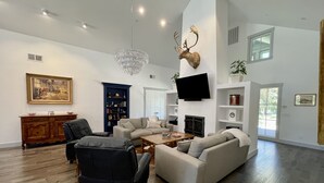 A spacious living room with a fireplace, a mounted deer head, a chandelier, and a large painting on the wall.