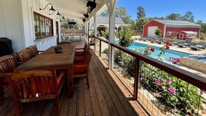 A covered outdoor deck with wooden furniture and a pool in the background.