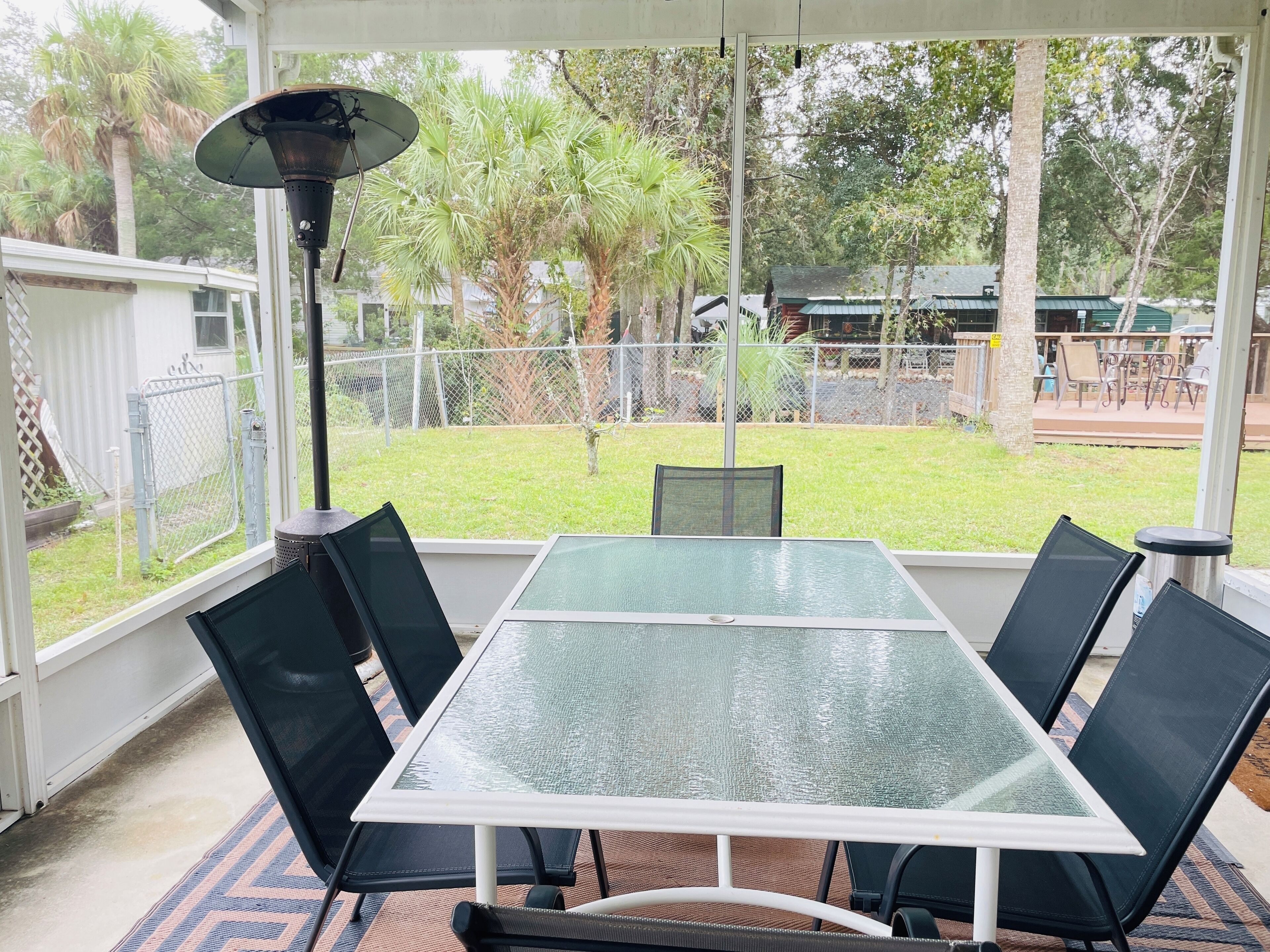 A covered patio with a glass table and chairs, a metal fence, and trees in the background.