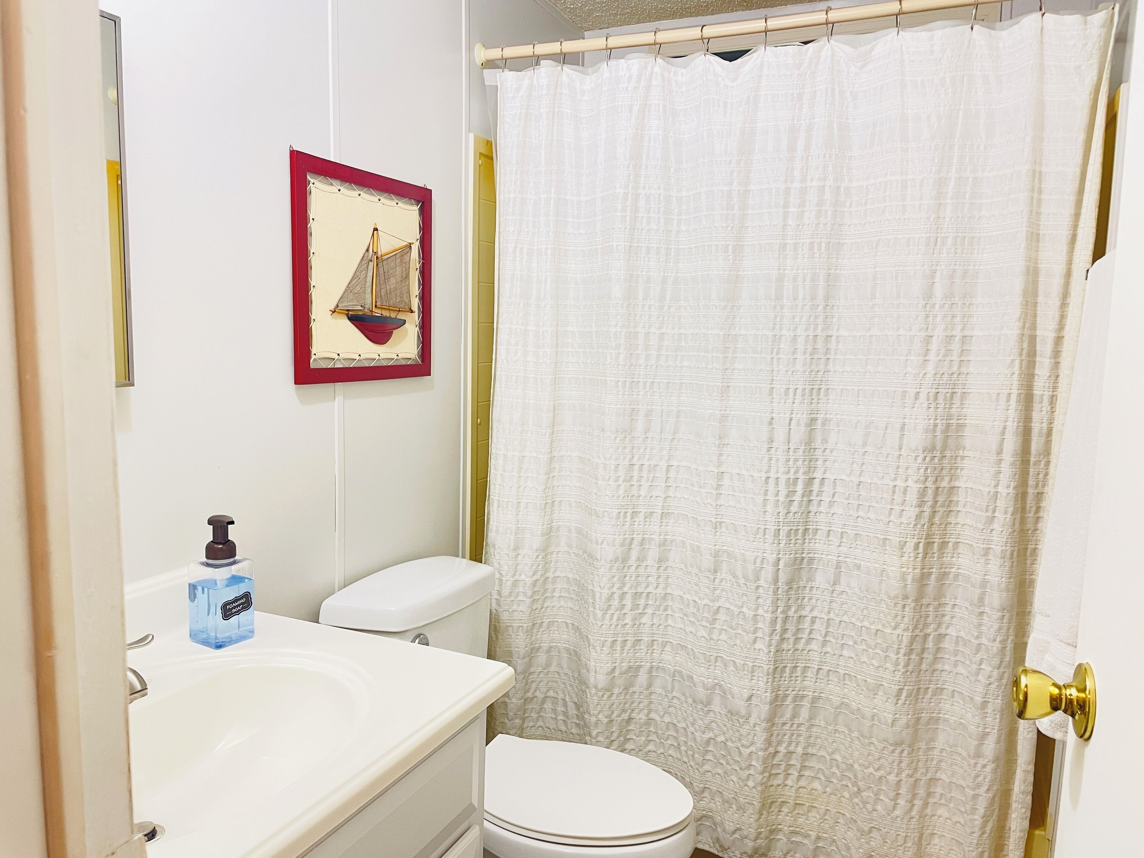 Une salle de bain avec des toilettes blanches, un lavabo doté d’un distributeur de savon et un rideau de douche.
