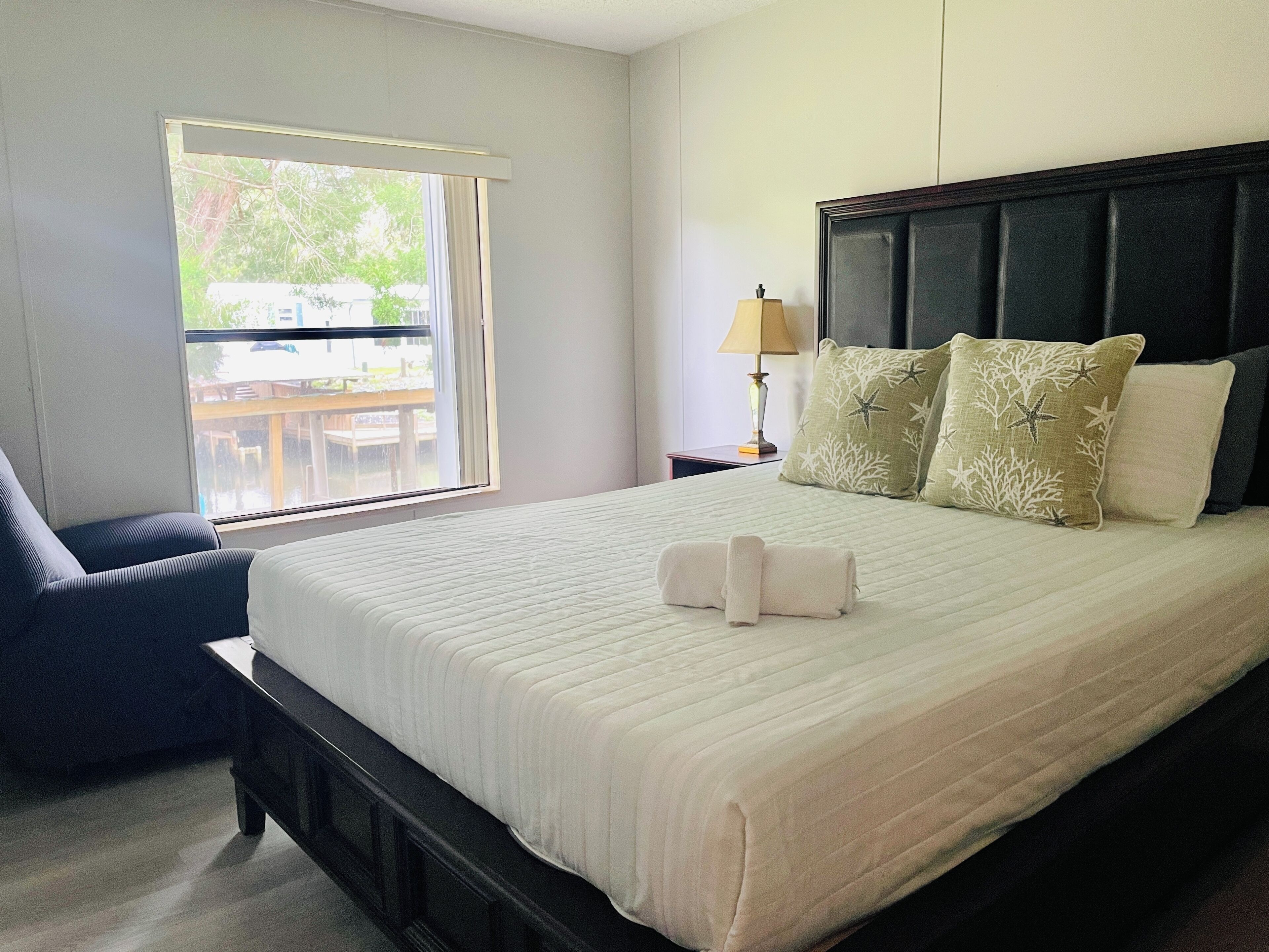 Un lit bien fait, avec une couette blanche, une tête de lit foncée et deux coussins décoratifs.