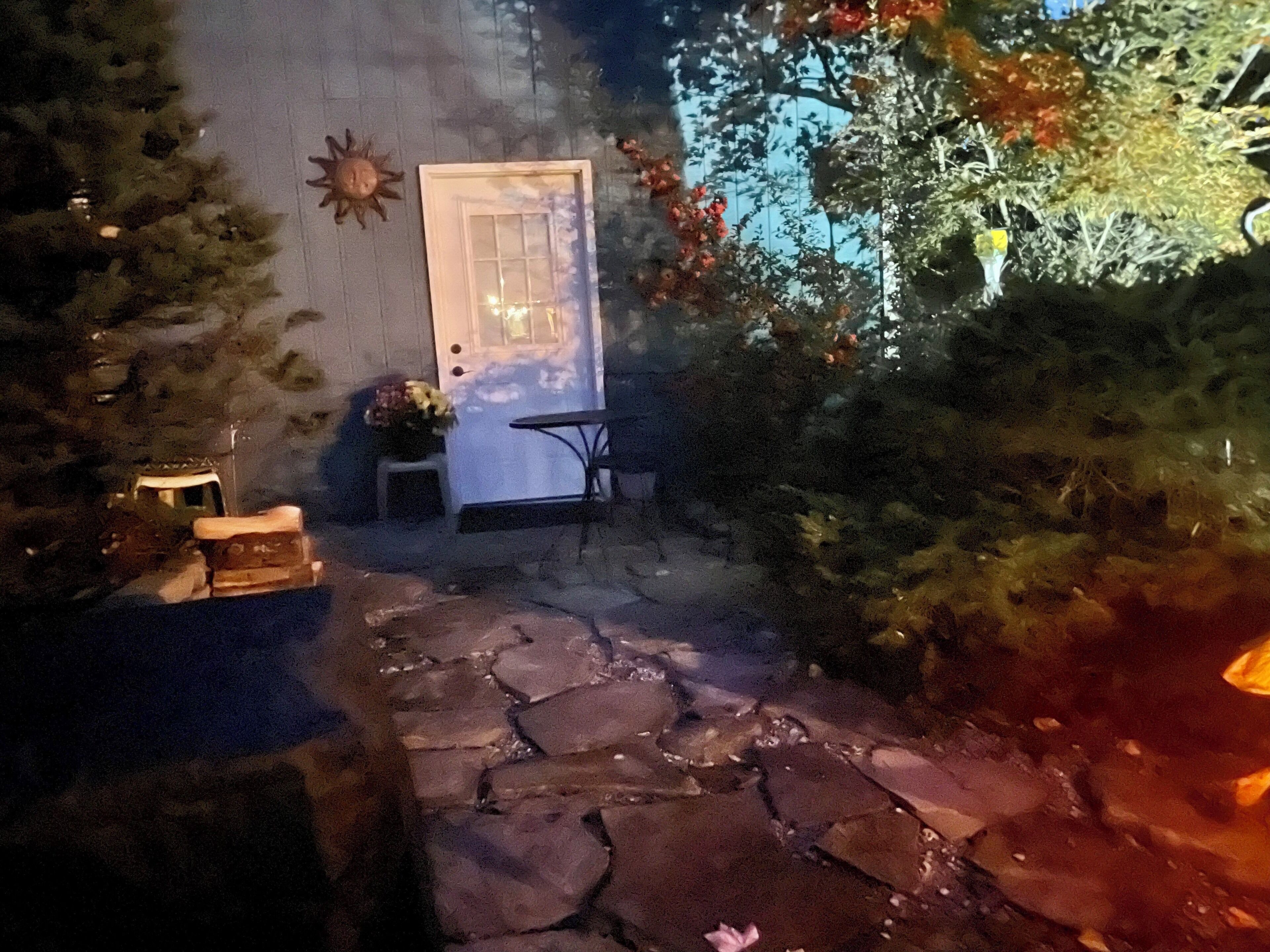 Ein Steinweg führt zu einer Tür, vor der sich ein kleiner Tisch und ein Stuhl befinden.