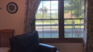 A room with a large window, a leather chair, a wall clock, and a radiator. - Cozy Buckhannon Cottage, Panoramic Views, Koi Pond & Close to Town (Buckhannon)