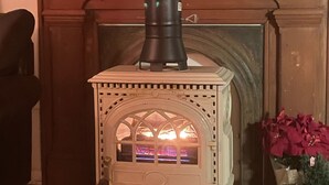 A white wood-burning stove with a glass door, positioned in front of a fireplace with a decorative mantel. - Cozy Buckhannon Cottage, Panoramic Views, Koi Pond & Close to Town (Buckhannon)