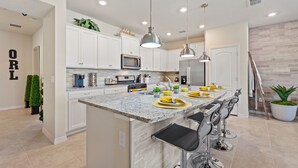 A modern kitchen with white cabinets, granite countertops, stainless steel appliances, and bar seating.