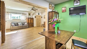 Ein geräumiger Wohnbereich mit Holzboden, einer Couch, einem Esstisch mit Blumenvase und einem an einer grünen Wand befestigten Fernseher.