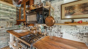 A rustic kitchen with a stone wall, wooden cabinets, and a hanging pot rack. - Wilderness Country Inn: France (Mentone)