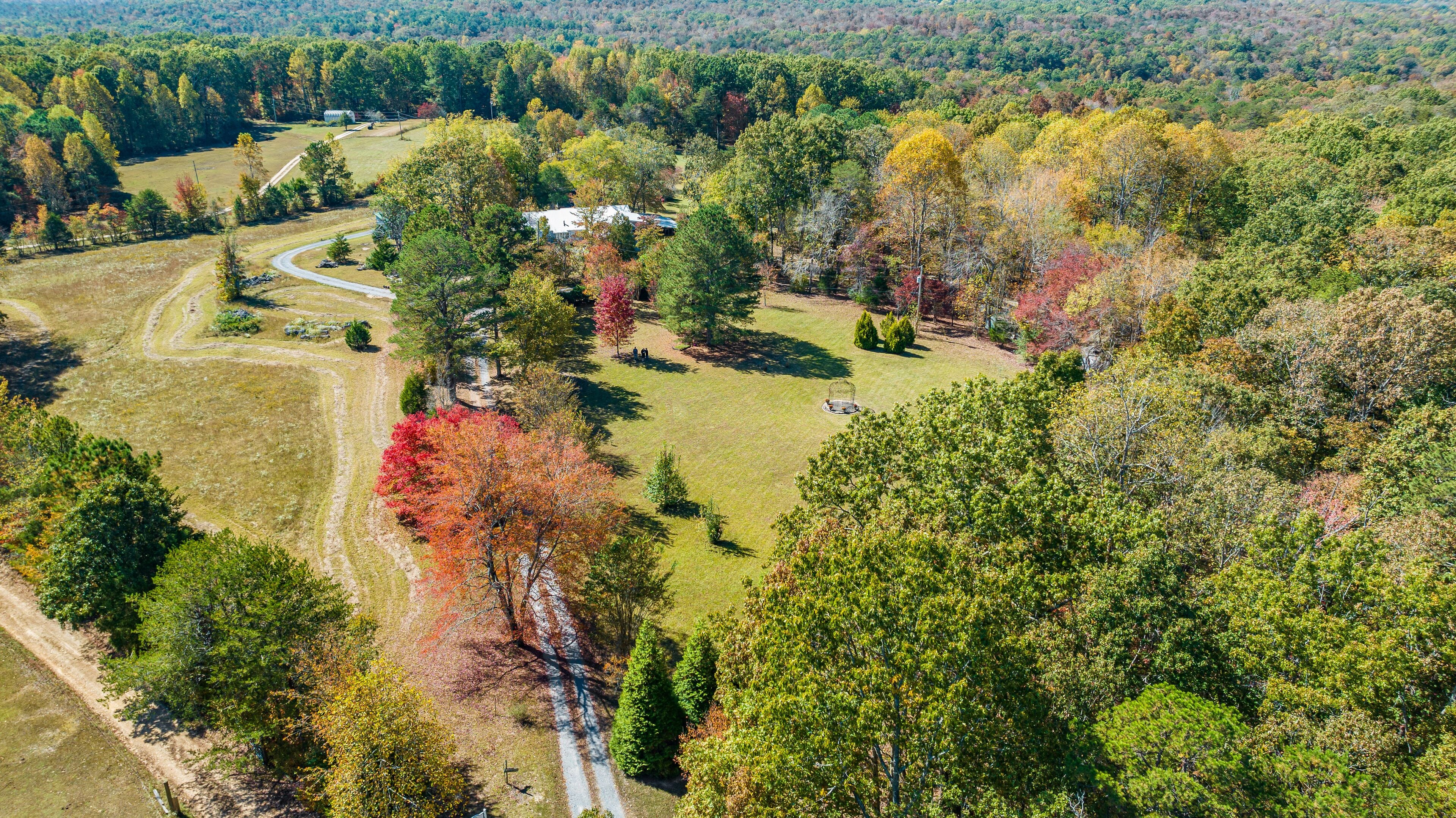 Vue aérienne d’une propriété rurale avec un chemin sinueux, une petite maison et des arbres environnants.