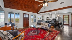 A spacious living area with a large wooden ceiling, a red patterned rug, and a modern kitchen in the background. - Texas Hill Country Escape in Hye, TX (Hye)