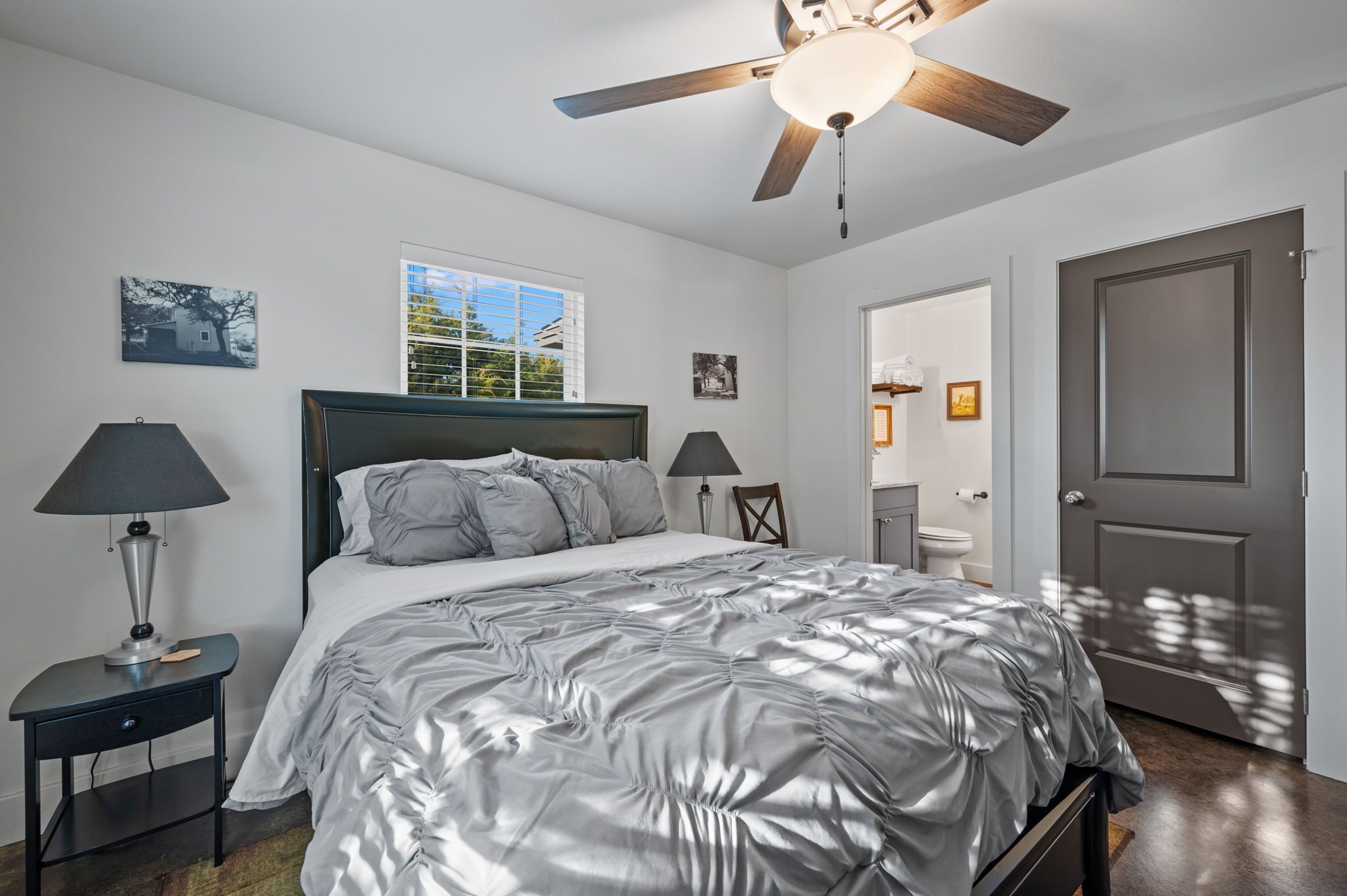 Une chambre à coucher avec un lit, deux tables de chevet avec des lampes, un ventilateur de plafond et une porte.