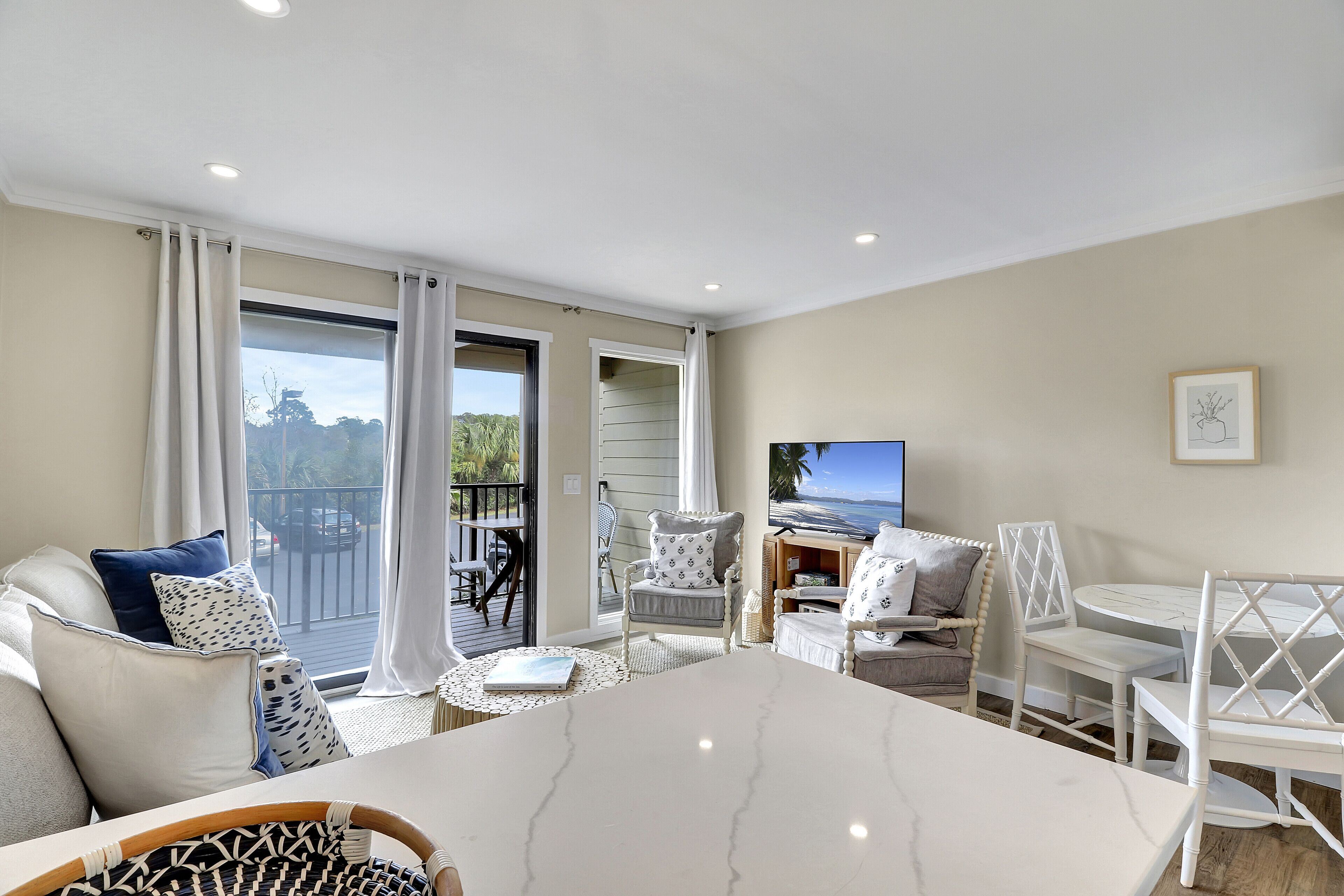 A modern living room with a marble table, white and patterned chairs, a sofa with blue and white cushions, and a television.