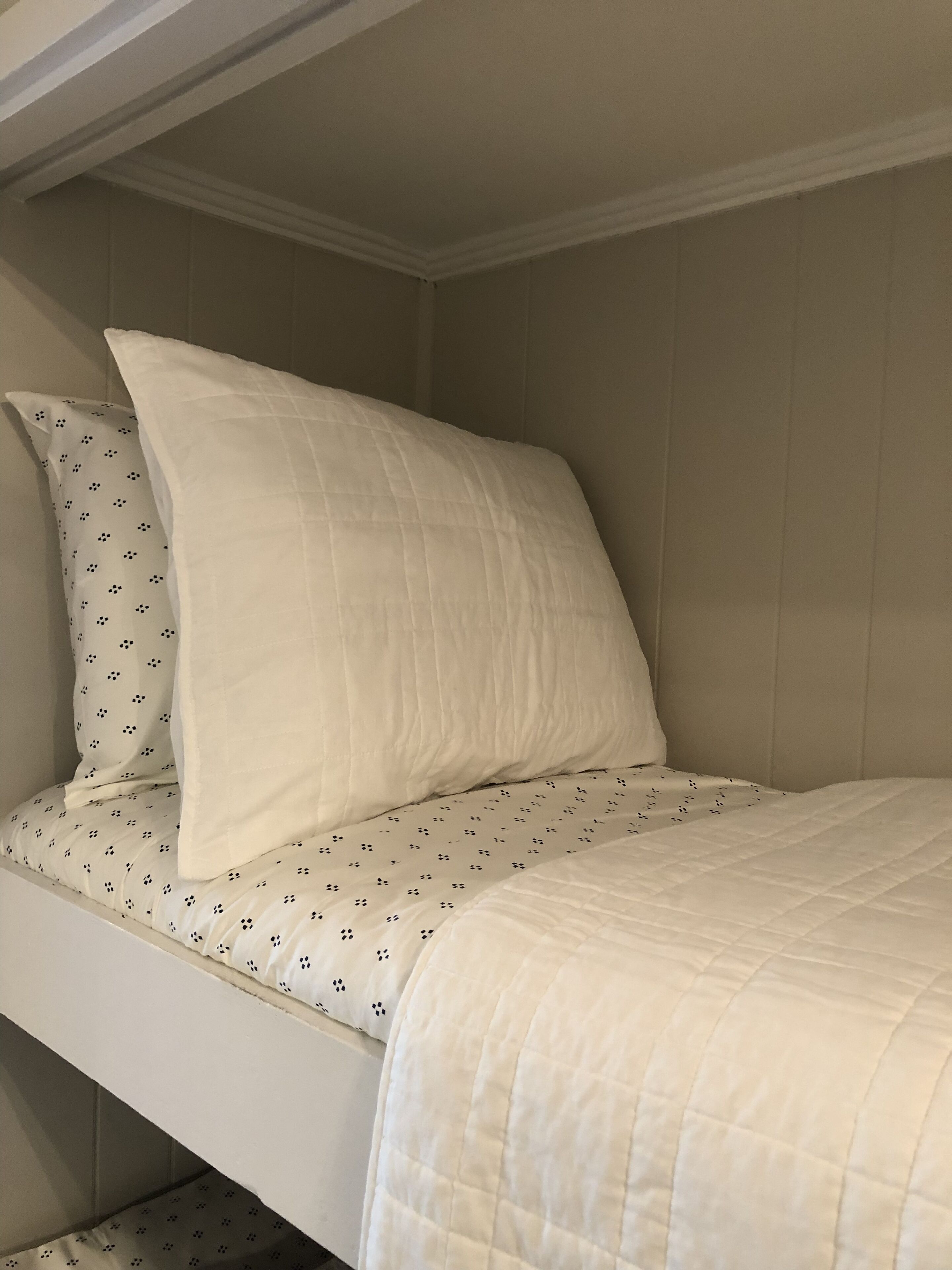 A bunk bed with a white quilted mattress and a patterned pillow.