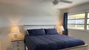 Ein Schlafzimmer mit einem Bettgestell aus Holz, einem Deckenventilator und einem Fenster mit Vorhängen.