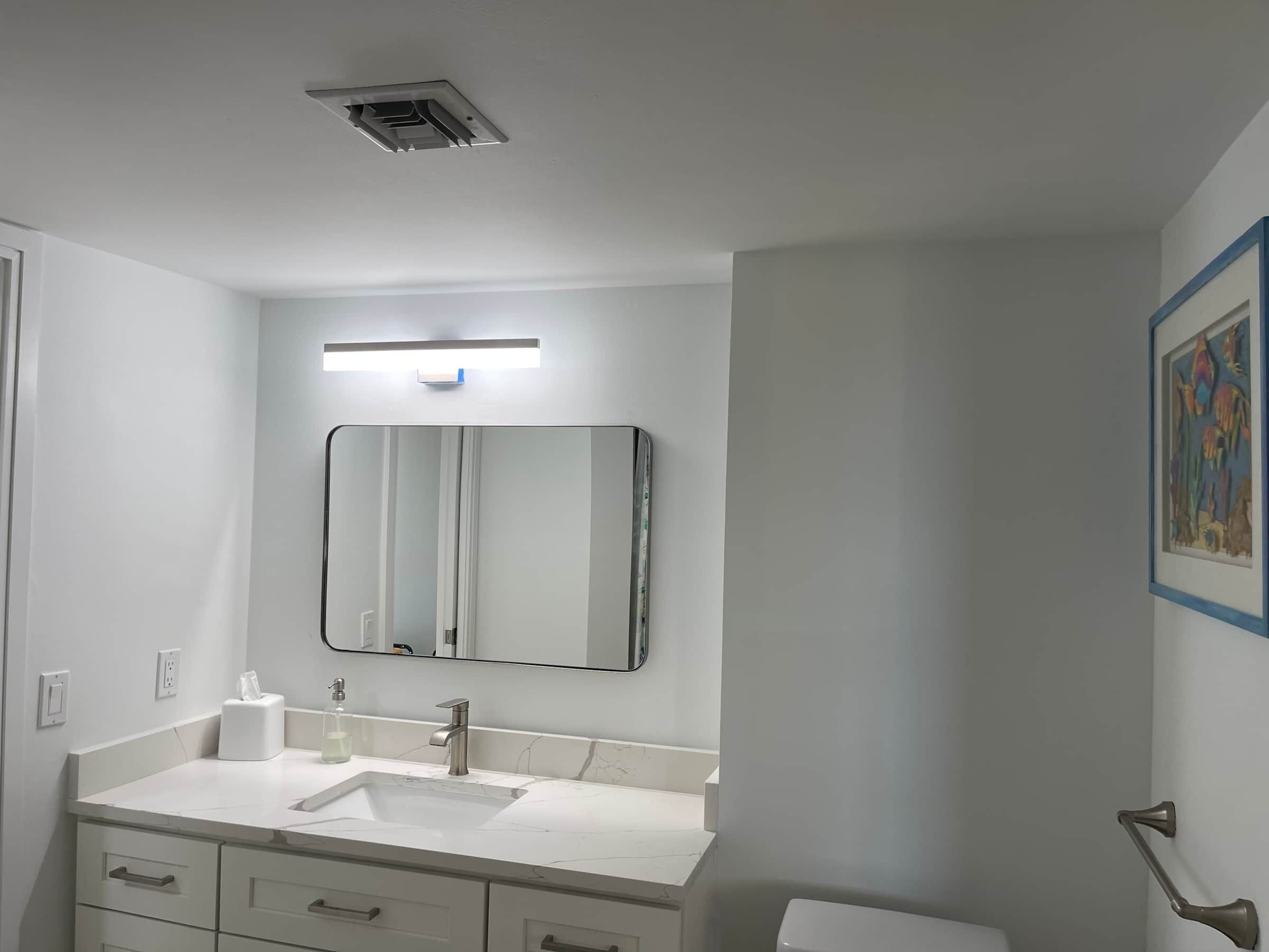Un baño con lavamanos blanco, un espejo, una lámpara sobre el espejo y un inodoro.