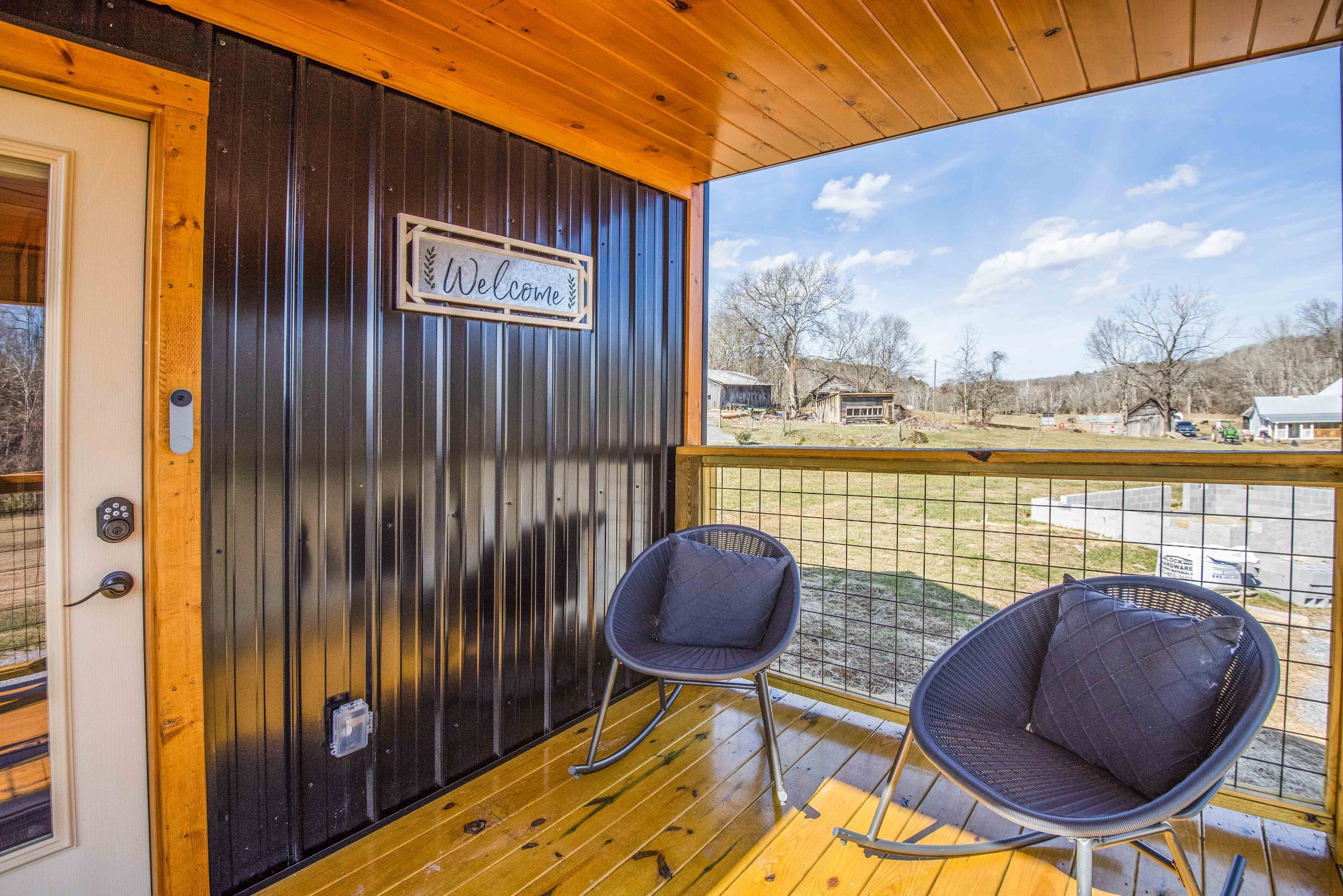 A wooden deck with two rocking chairs and a 'Welcome' sign on a metal wall.