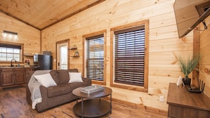 L’intérieur d’un chalet en bois comprend un espace de vie avec un canapé, une table basse et une cuisine dotée de meubles en bois et d’un réfrigérateur.