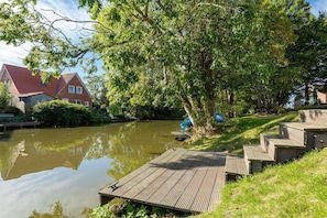 Una propiedad junto al río con un muelle de madera, una casa con techo rojo y abundante vegetación.