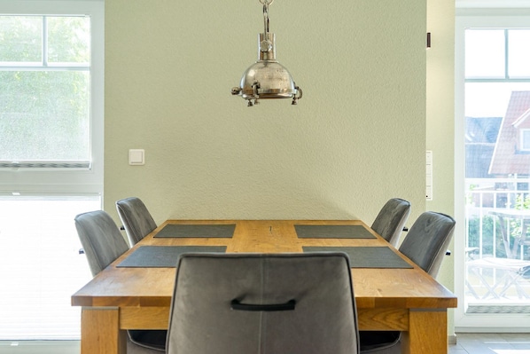 Comedor con mesa de madera, seis sillas, lámpara colgante y ventanas amplias.