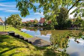 A calm water body with a wooden dock, surrounded by greenery and houses in the background.