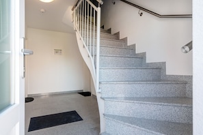 Un escalier avec une rampe, une porte donnant sur une pièce et un tapis noir sur le sol.