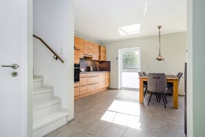 A modern kitchen with wooden cabinets, a dining area with a table and chairs, and a staircase leading to another level.