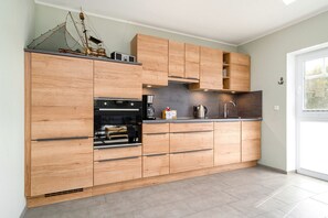 A modern kitchen with wooden cabinetry, a built-in oven, and a coffee maker.