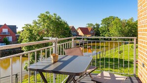 Ein Balkon mit Tisch und Stühlen, einem Metallgeländer und Blick auf einen Kanal mit Häusern im Hintergrund.