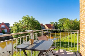 Ein Balkon mit Tisch und Stühlen, einem Metallgeländer und Blick auf einen Kanal mit Häusern im Hintergrund.