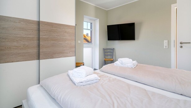 Ein Hotelzimmer mit zwei Betten, einem an der Wand montierten Flachbildfernseher, einer Holzvertäfelung an der linken Wand und Blick ins Freie durch ein Fenster.