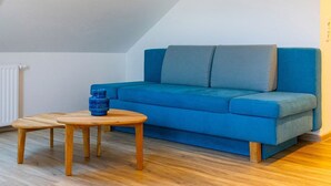 A blue sofa, two wooden tables, and a blue vase in a room with sloped ceilings and wooden flooring.