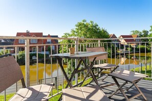 Eine Terrasse im Freien mit Tisch und Stühlen, mit Blick auf einen Kanal und Gebäude im Hintergrund.
