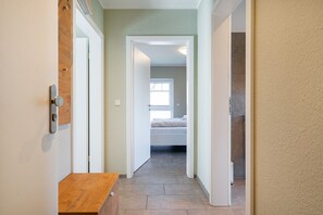A hallway leading to a bedroom with a bed, a wooden bench, and a door with a lock.