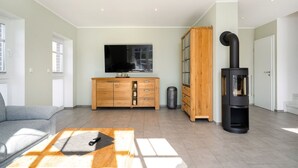 Ein modernes Wohnzimmer mit einer Couch, einem Holztisch, einem Fernseher, einem Schrank und einem Kaminofen.