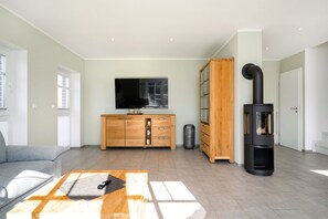 A modern living room with a sofa, a wooden coffee table, a TV, a cabinet, and a wood-burning stove.