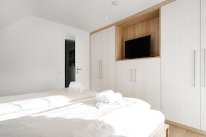 Une chambre à coucher moderne, avec un lit, un téléviseur fixé sur un meuble en bois et une porte donnant sur une autre pièce.