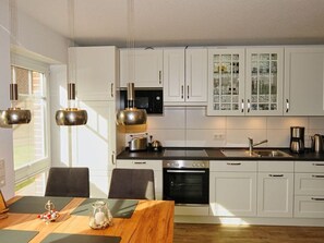 A modern kitchen with white cabinets, a black stove, and a dining area with a wooden table and chairs.