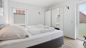 A modern bedroom with a bed, a wardrobe, a mirror, and a ceiling light fixture.