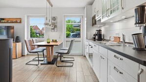 A modern kitchen with white cabinets, a stainless steel range hood, and a dining area with a table and chairs.
