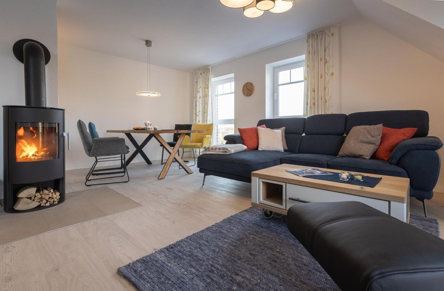 A modern living room with a wood-burning stove, a sofa, a coffee table, and a dining area with chairs.