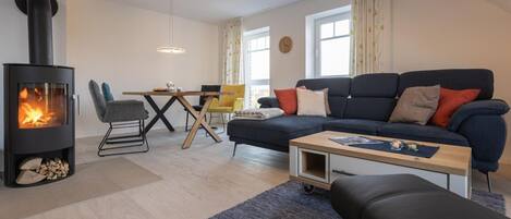 A modern living room with a wood-burning stove, a sofa, a coffee table, and a dining area with chairs.