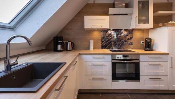 A modern kitchen with a skylight, built-in oven, and white cabinetry.
